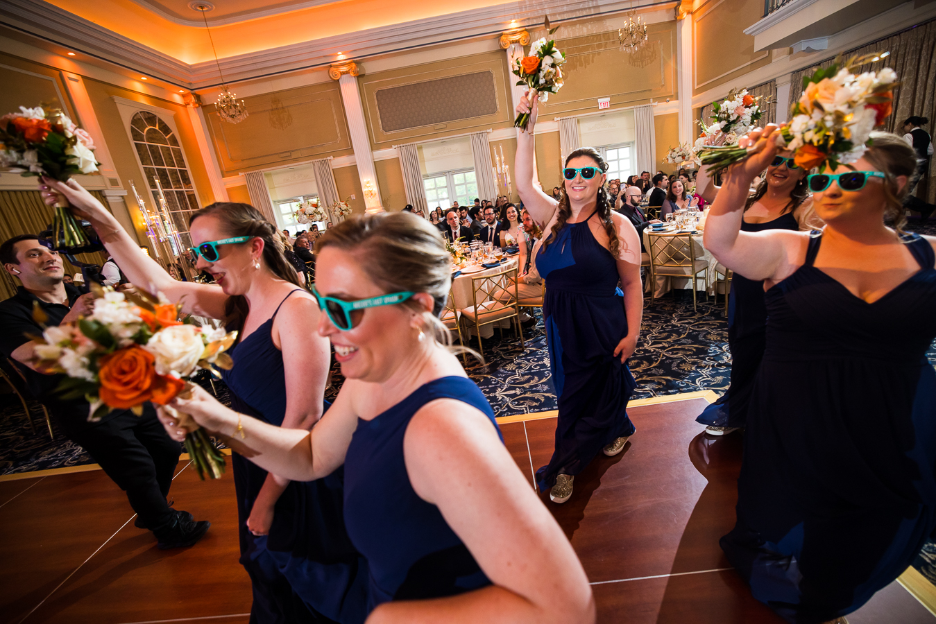 new jersey wedding photographer, lisa rhinehart, captures this unique perspective of the bridesmaids as they enter into the wedding reception together with their bouquets in the air and sunglasses down 