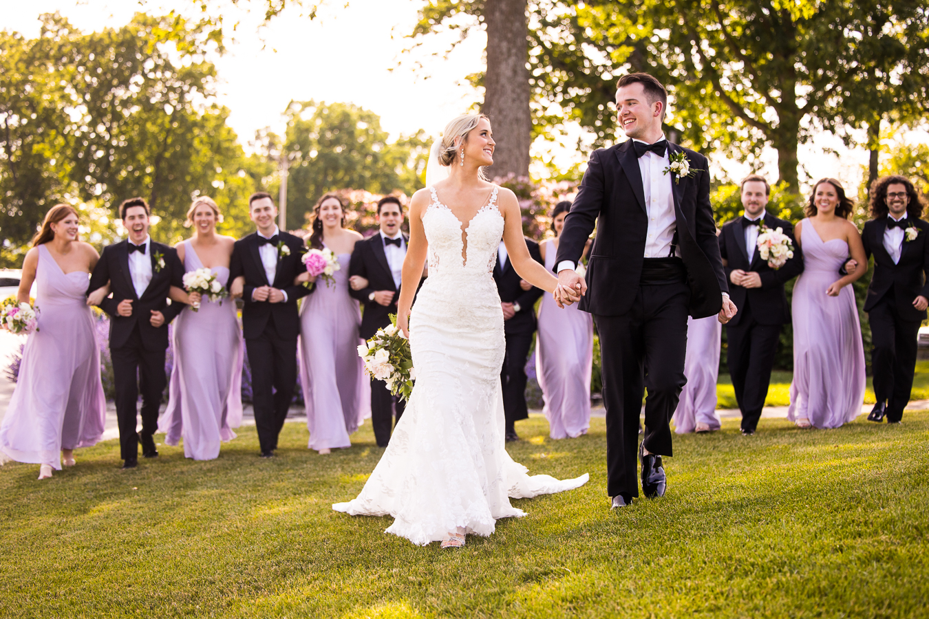 Bride and groom walking infront of their lilac dress wedding party during their wedding party portraits at their Country Club of York Wedding