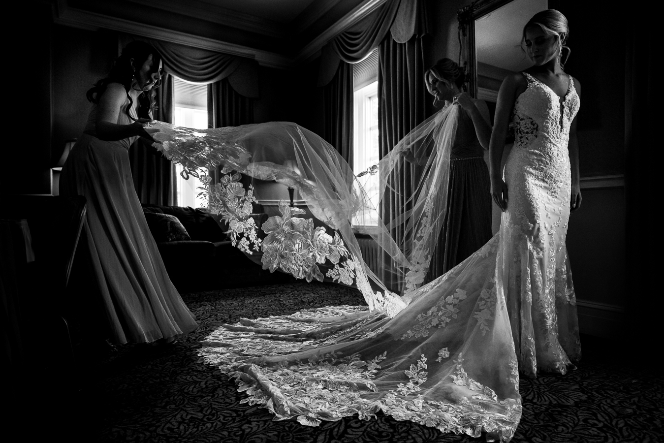creative wedding photographer, lisa rhinehart, captures this black and white image of the bride standing in her wedding dress as her bridesmaids lay out her train for her