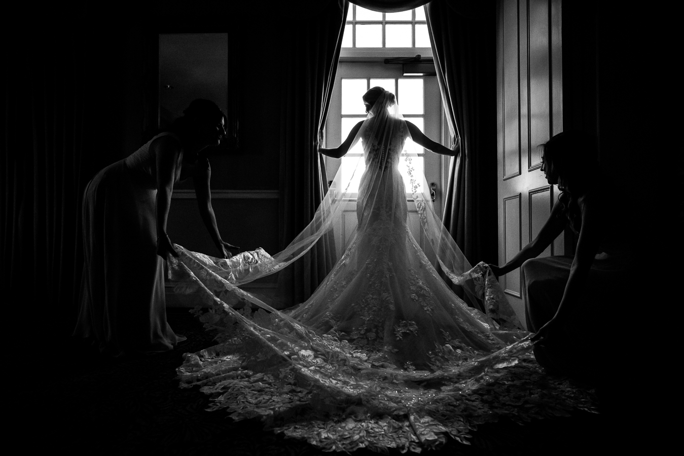 Country Club of York Wedding photographer, rhinehart photography, captures this stunning black and white image of the bride as she stands in the window while her bridesmaids fix her dress