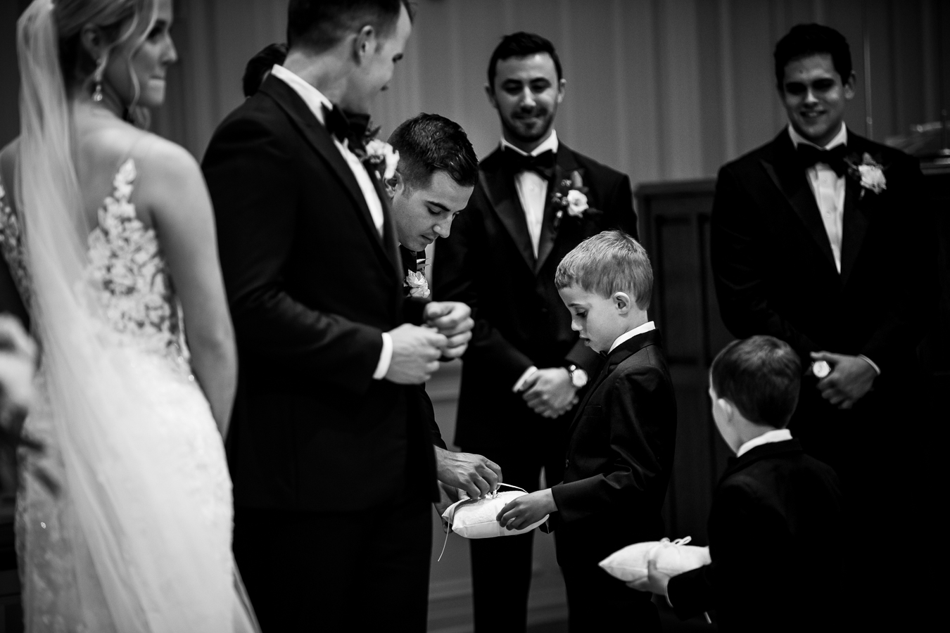 creative black and white image of the ring bears as they pass the rings off to the best man during the wedding ceremony