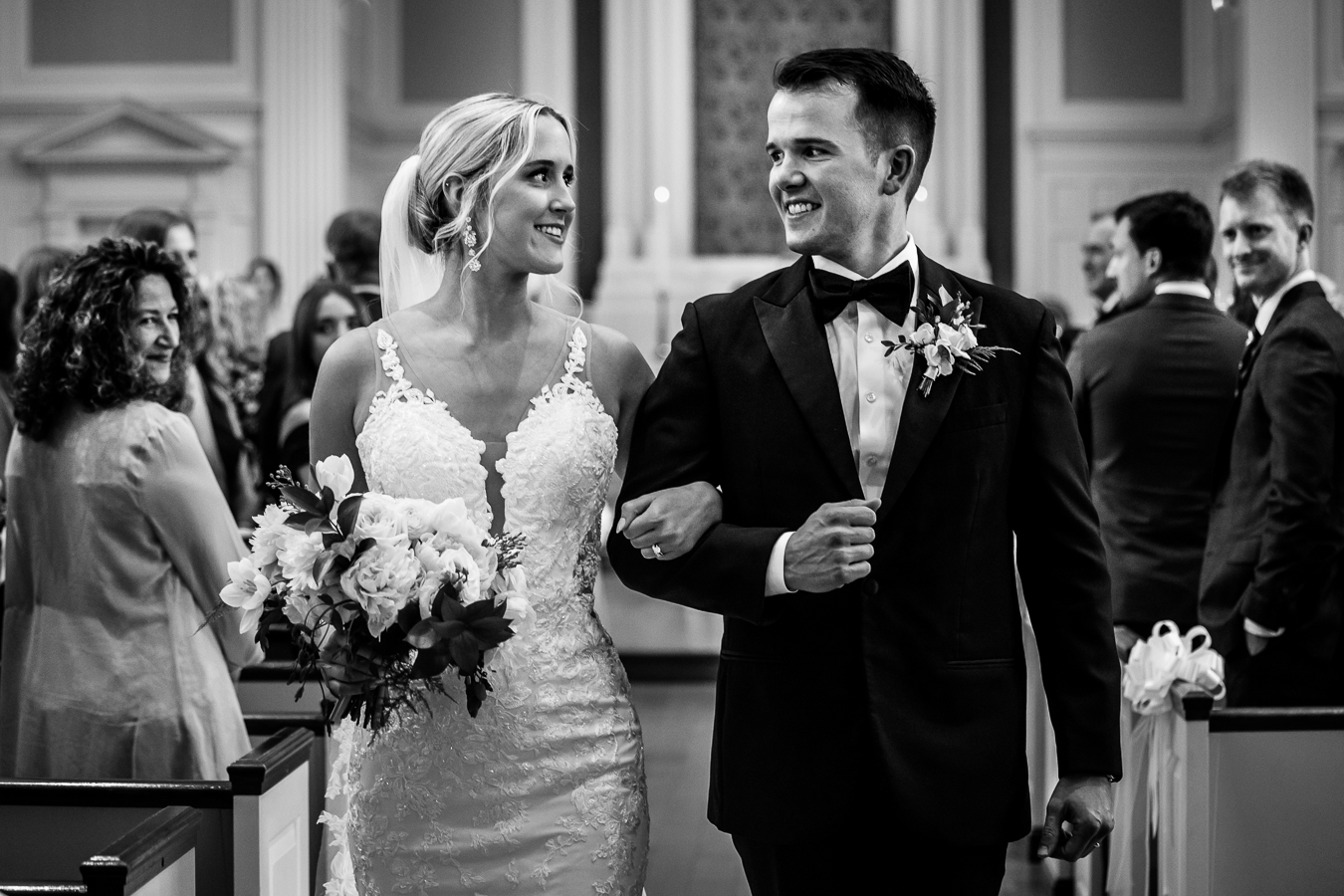 black and white image of the bride and groom as they walk down the aisle together as husband and wife with their arms locked together for their st pauls lutheran church wedding ceremony