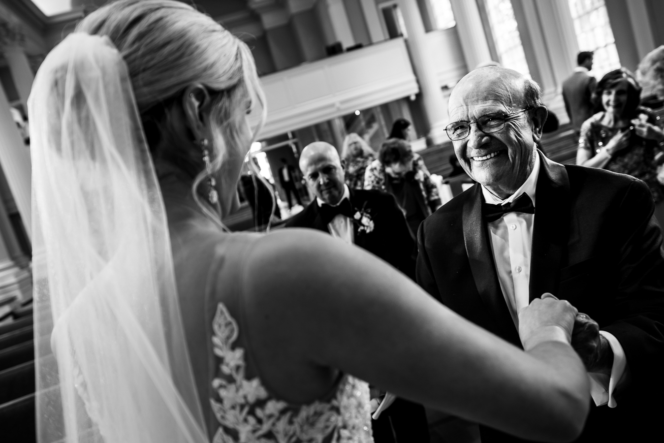black and white image of the bride holding hands with a guest as they are smiling big at her