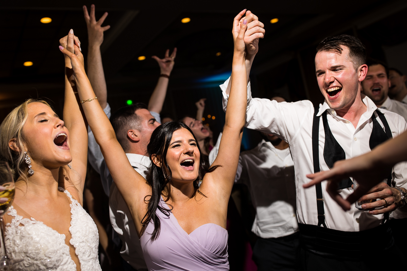 imge of the bride and groom holding hands with a bridesmaid with their arms in the air as they sign and dance on the dancefloor at this country club of york wedding