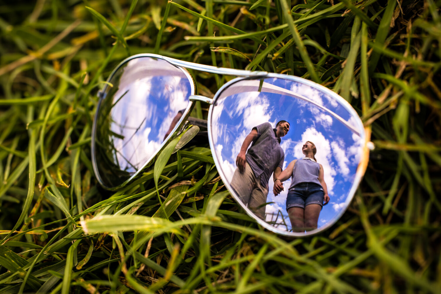 Creative Proposal Photographer, rhinehart photography, captures this creative, fun, unique image of the couple holding hands and exploring caught through the reflection on the sunglasses lens in st louis