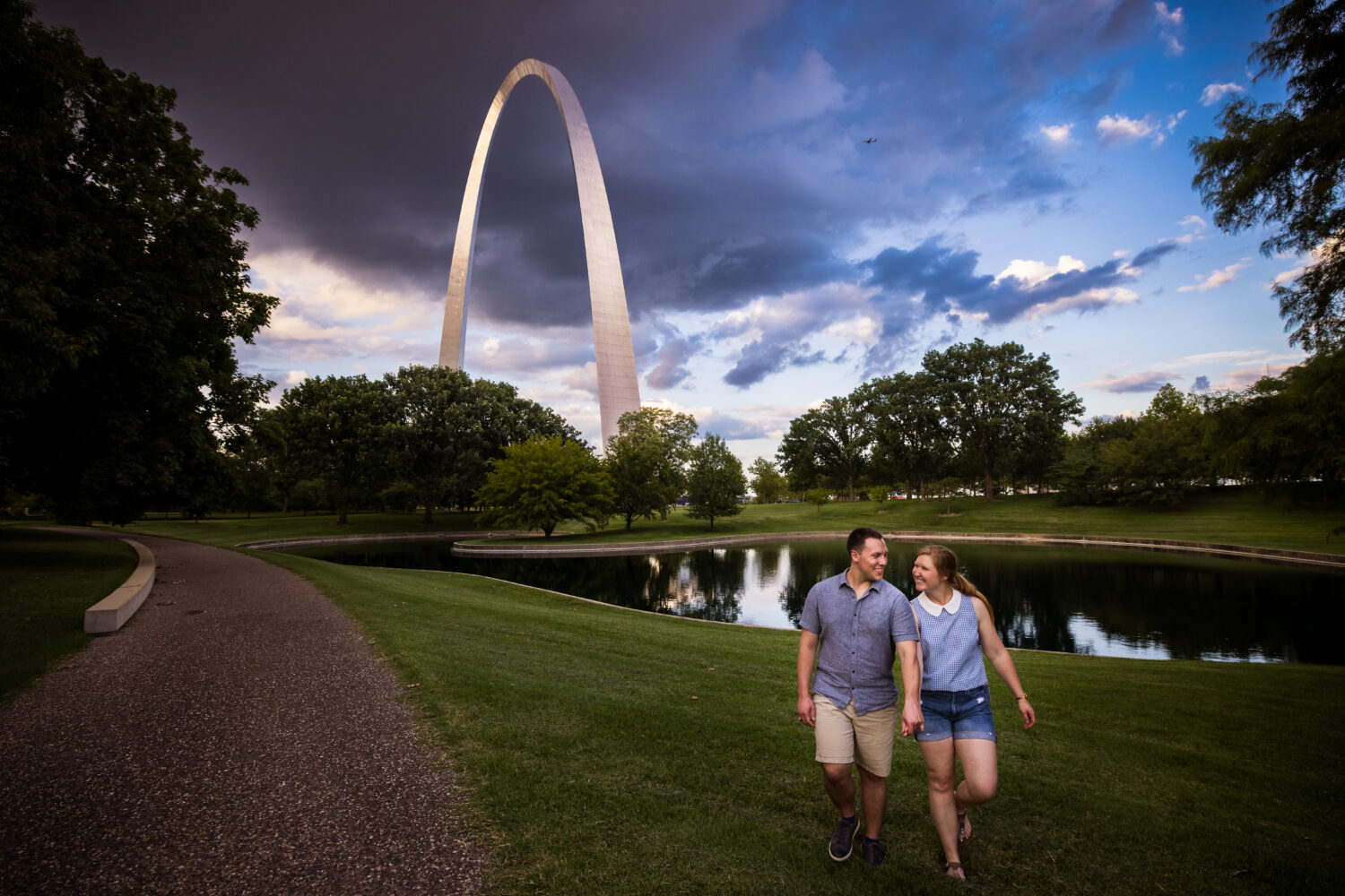 Creative Proposal Photographer, rhinehart photography, captures this unique perspective of the couple holding hands, smiling at one another with the archway in the background behind them as a storm gets ready to roll in 