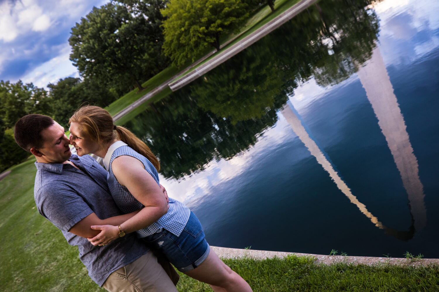 Creative Proposal Photographer, lisa rhinehart, capture this creative, unique, fun image of the couple as they hug and smile at each other with the archway in the background behind them captured in the reflection of the pond behind them 