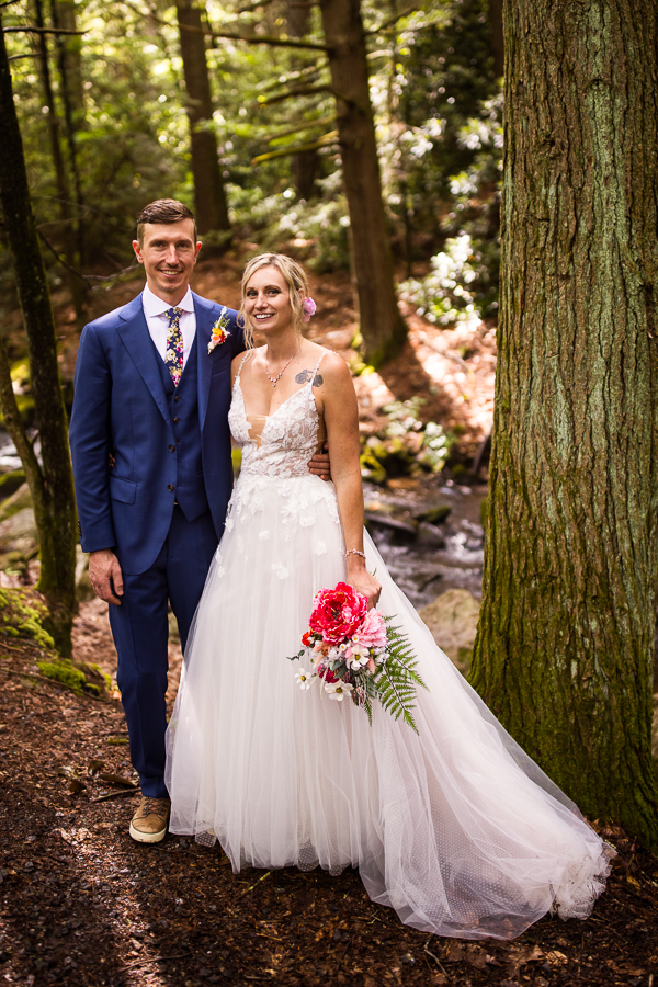 micro wedding photographer, lisa rhinehart, captures this traditional portrait of the bride and groom standing beside one another surrounded by nature, trees and a stream for their romantic portraits 