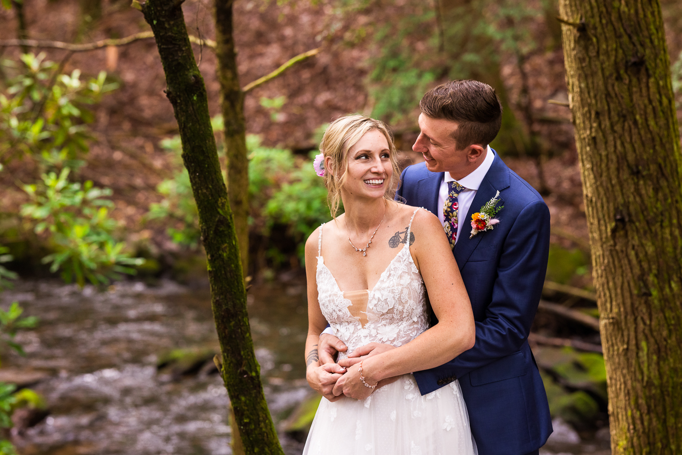 jim thorpe micro wedding photographer, lisa rhinehart, captures this romantic image of the bride and groom hugging one another and smiling as they have a stream, trees and nature behind them on this pa hiking trail