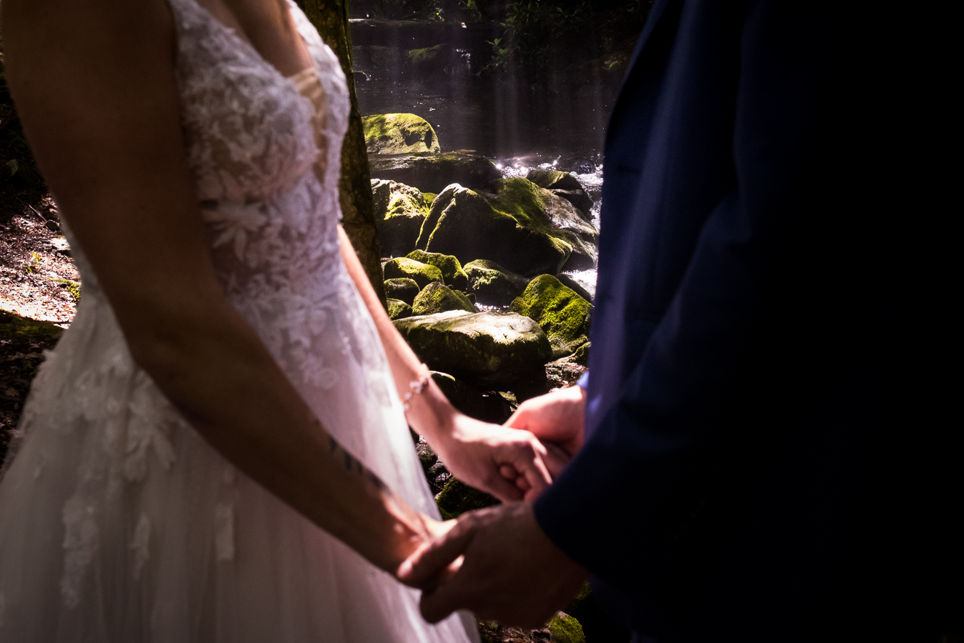 image of the bride and groom holding hands surrounded by the nature, stream and trees around them 