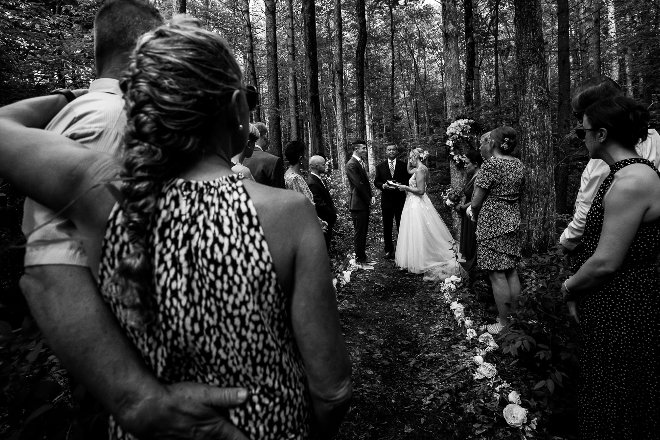 jim thorpe wedding photographer, lisa rhinehart, captures this black and white image of the bride and groom standing at the end of the aisle surrounded by friends and family for their intimate wedding ceremony