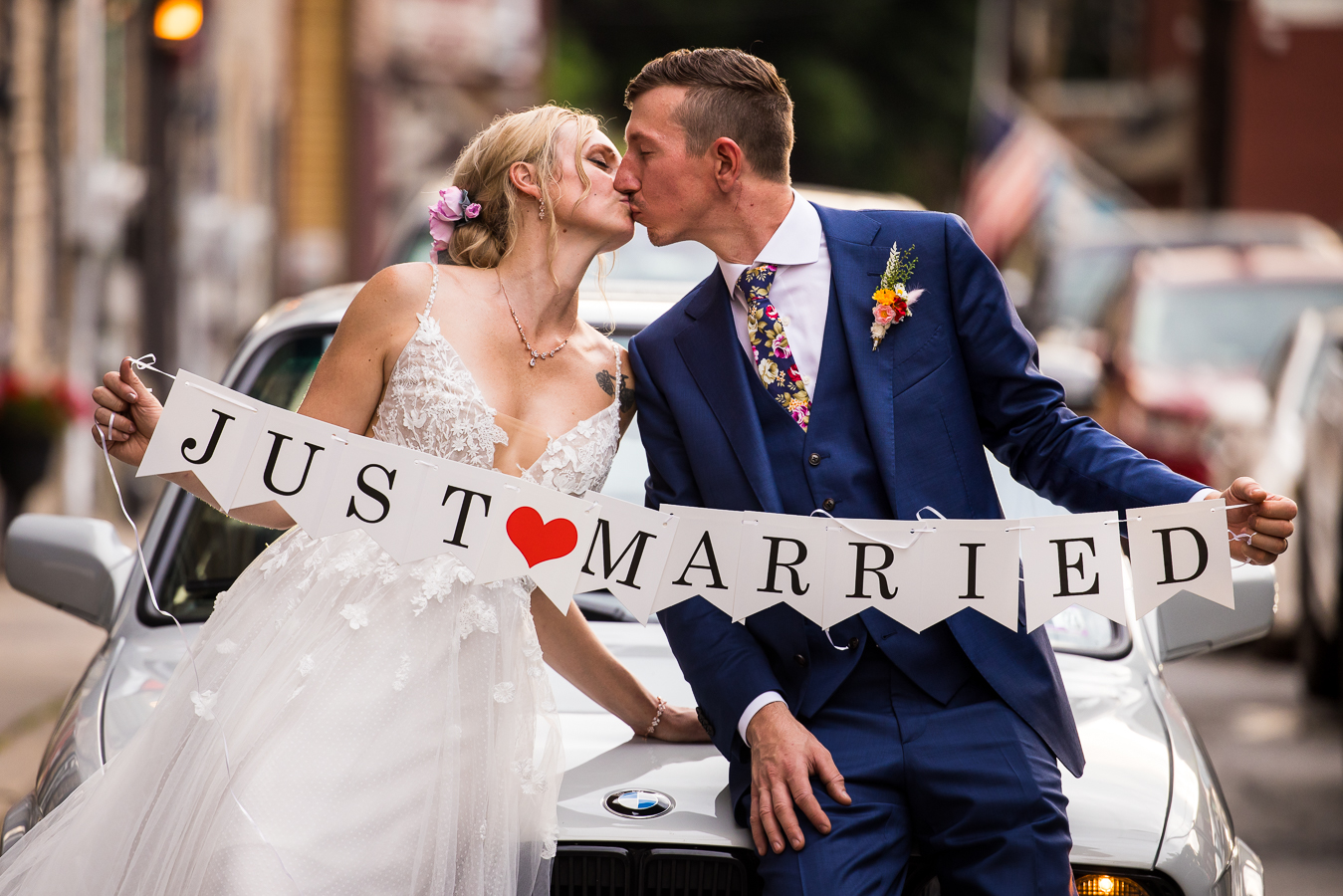 best pa wedding photographer, lisa rhinehart, captures this fun image of the bride and groom kissing one another after their wedding ceremony holding a sign saying just married as they sit on the front of a car 