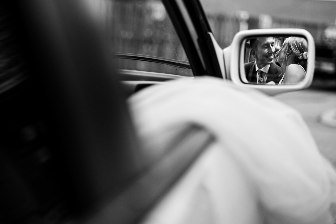 creative wedding photographer, lisa rhinehart, captures this creative, fun black and white image of the bride and groom leaning in to kiss one another captured through the mirror of the car they are leaving in after their wedding ceremony 