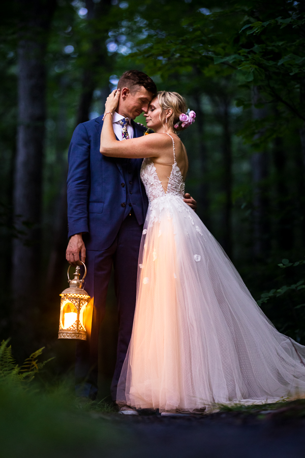 magical, creative image of the bride and groom as they embrace one another while holding a lantern inside the woods on the hiking trail