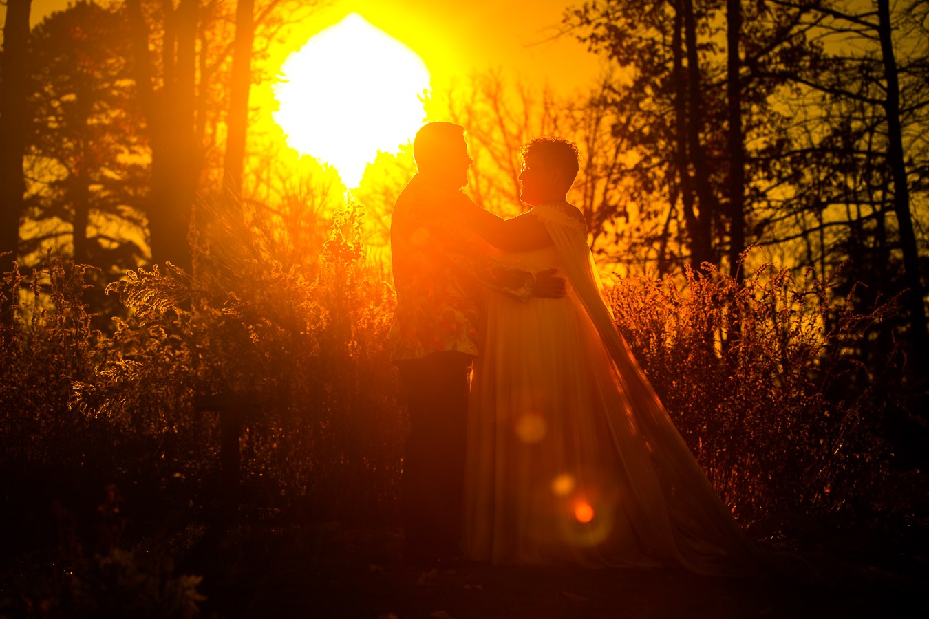 Washington DC LGBTQ Wedding Photographer, lisa rhinehart, captures this warm yellow orange image of the couple embracing each other in the woods as the golden sun sets behind them 