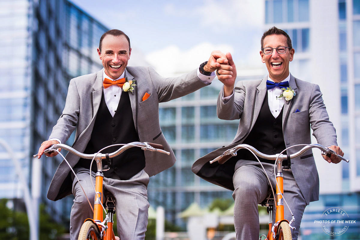 Fearless DC Wedding photographer, Lisa Rhinehart, captures this vibrant, colorful, fun image of the two grooms holding hands as they ride orange bikes before their wedding ceremony in DC