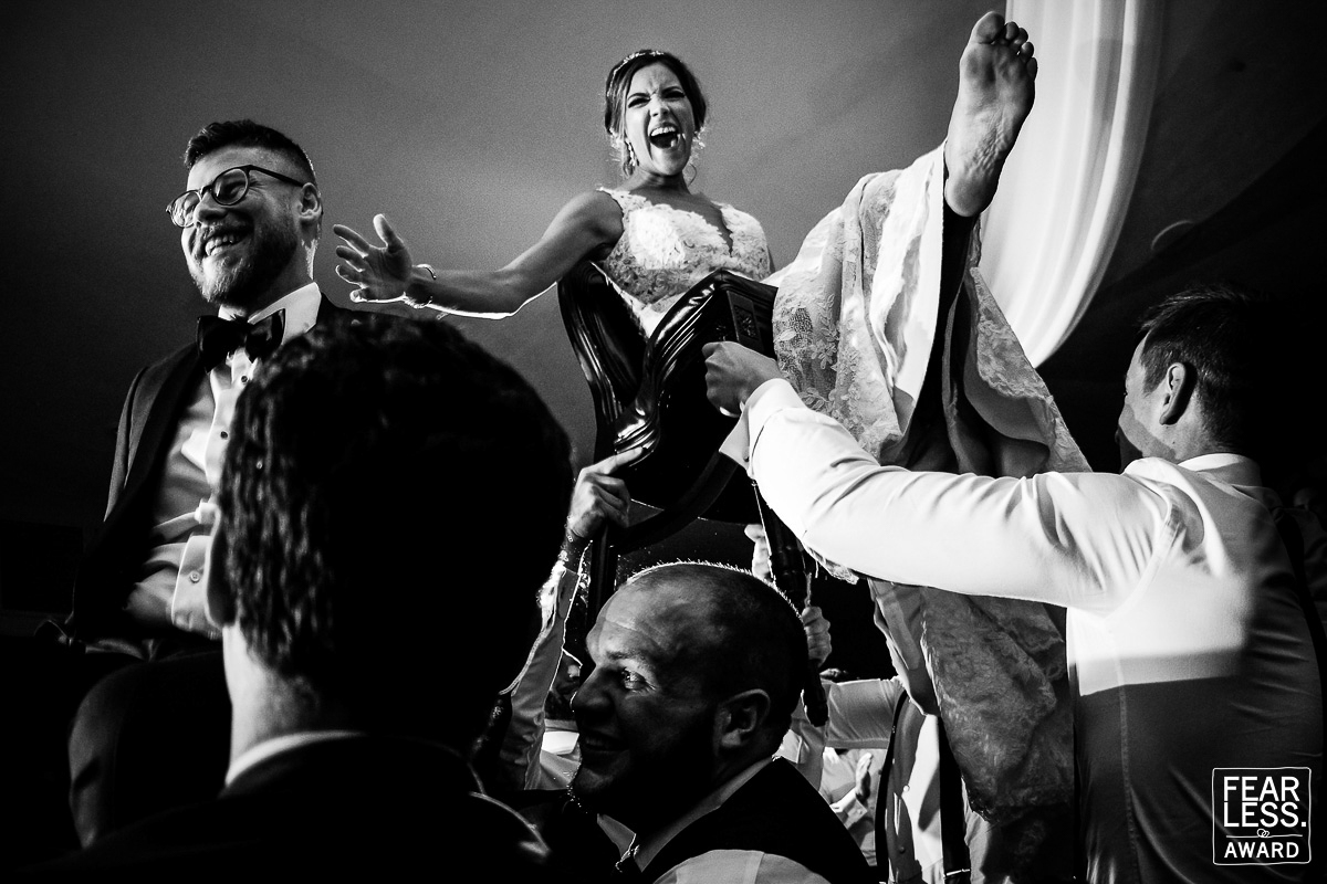 Fearless wedding photographer, lisa rhinehart captures this black and white image of the couple as they are lifted up on chairs with big smiles on their faces during their wedding ceremony