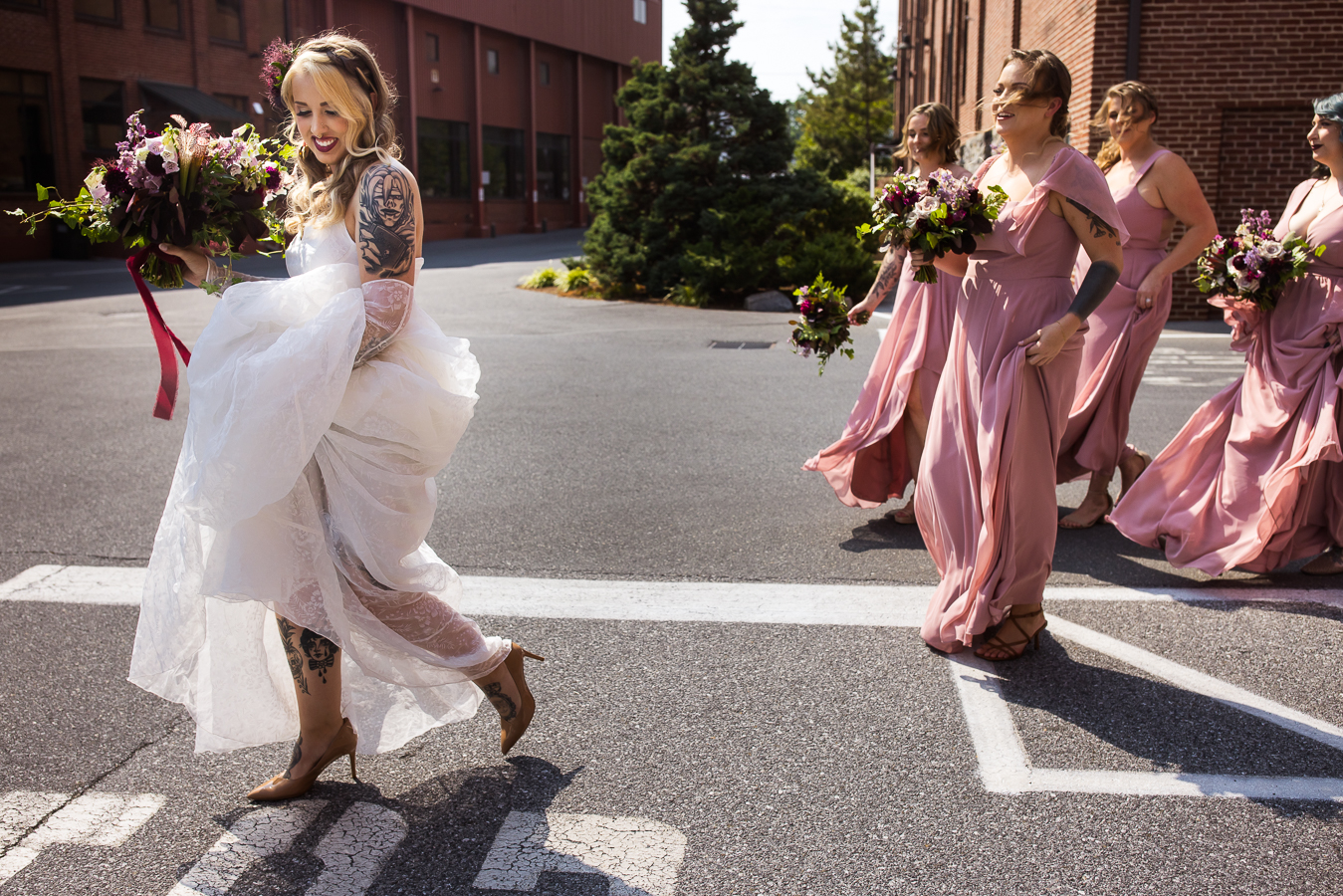 candid wedding photographer, lisa rhinehart, captures this image of the bride and her bridesmaids as they walk across the street holding up their dresses before the ceremony 
