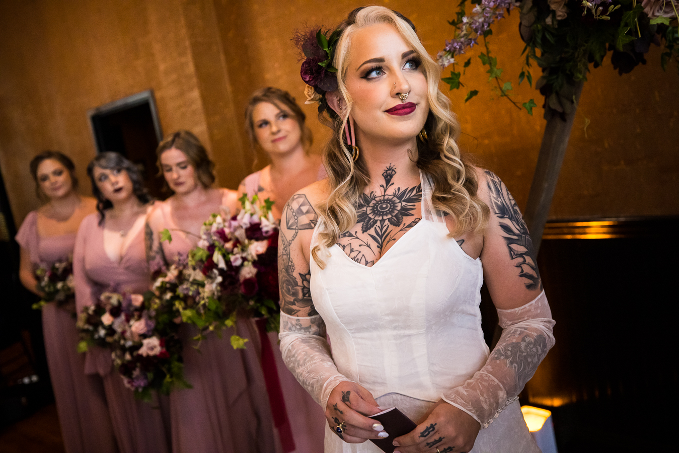 image of the bride as she smiles at the groom while he reads his vows with the bridesmaids behind her 
