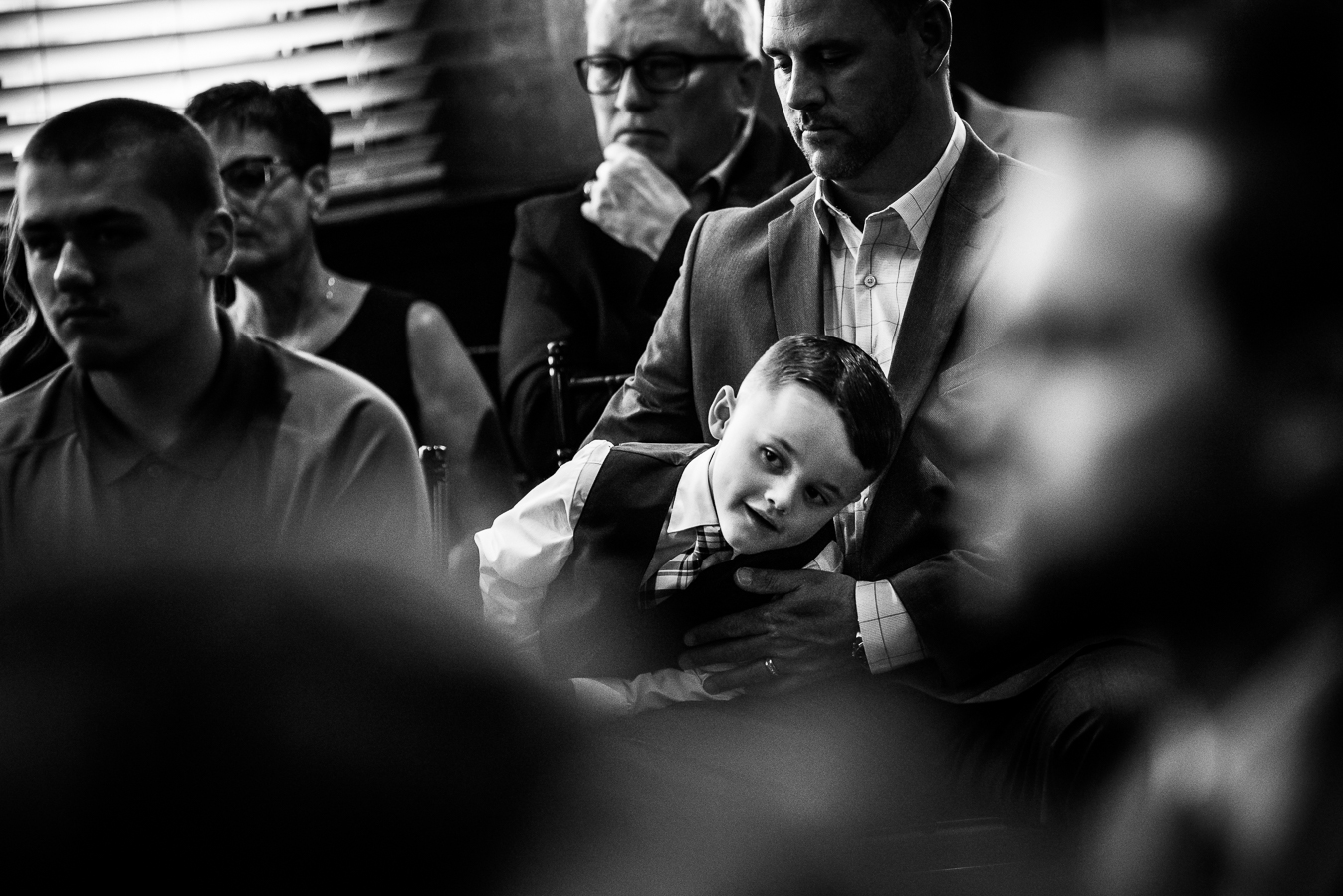 black and white image of a little boy leaning across his dad to watch the wedding ceremony in Lancaster pa 