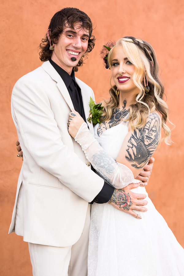 lisa rhinehart, captures this image of the bride and groom embracing one another while standing in front of a gorgeous terracotta colored wall for their wedding photos 