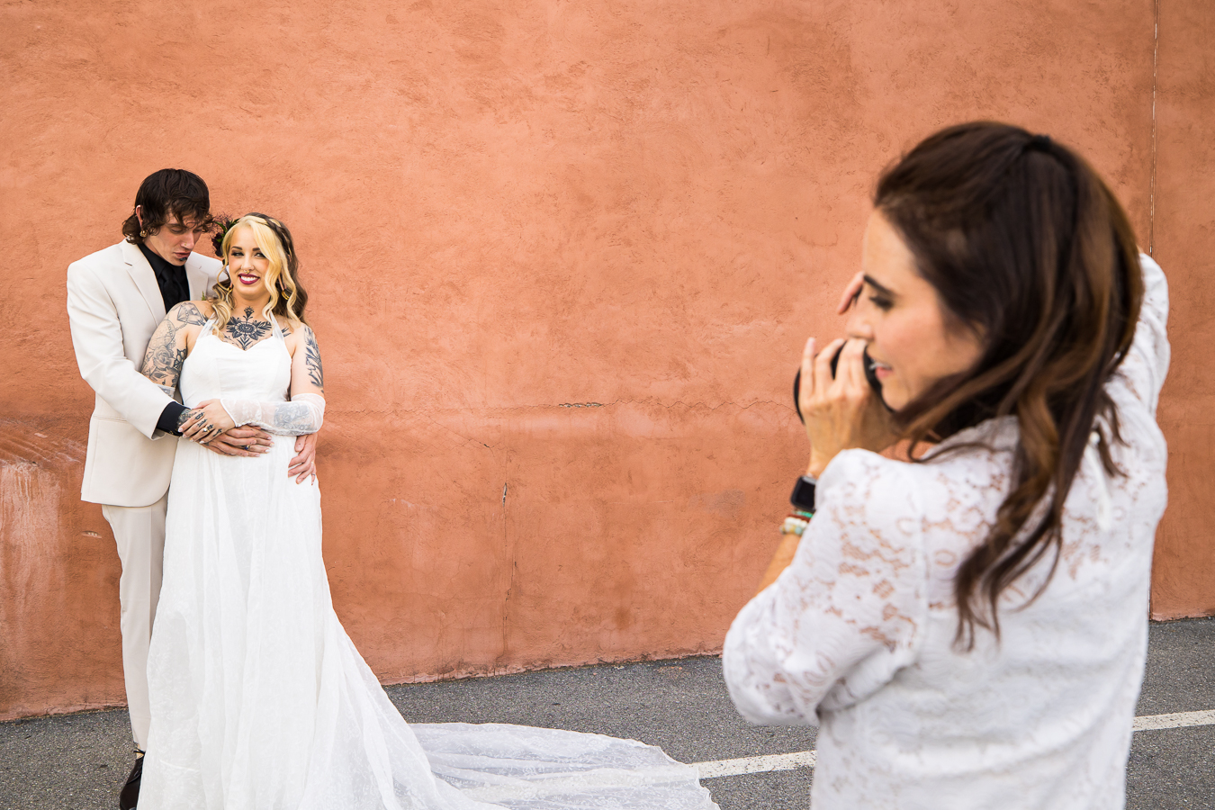 behind the scenes image of lisa rhinehart capturing the couple during their romantic portrait session in a parking lot against a terracotta colored wall
