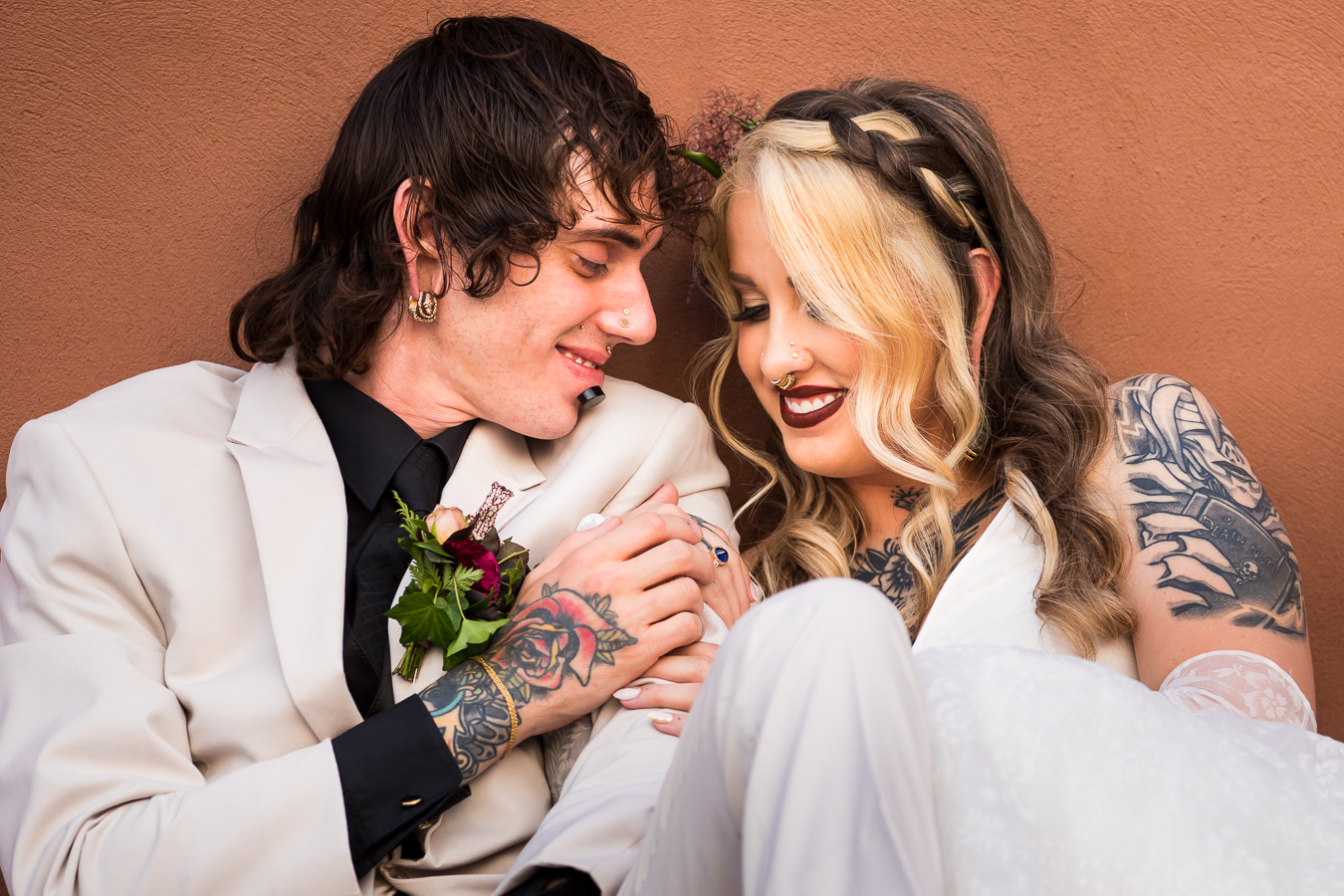 image of the bride and groom as they sit against the vibrant terracotta colored wall and smile at one another outside of their wedding venue in lancaster