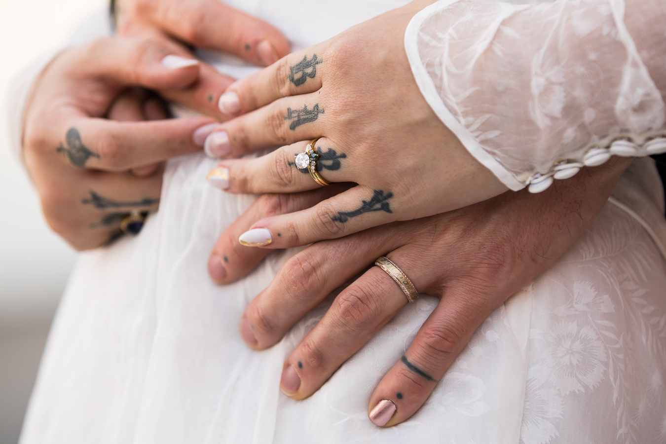 close up image of the bride and groom as they have their hands tangled with each others showing off their wedding rings and finger tattoos 