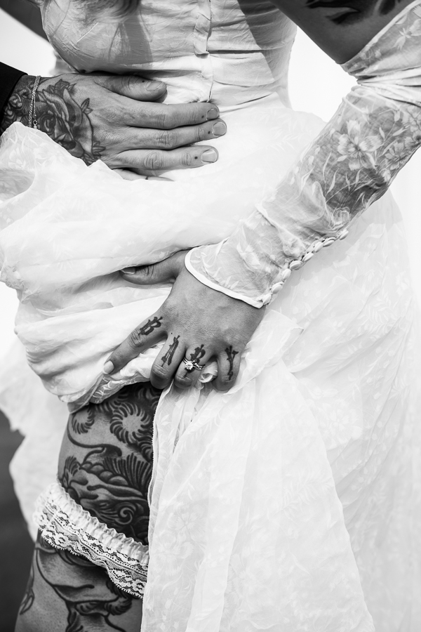 wedding photographer, lisa rhinehart captures this black and white image of the bride lifting her wedding dress and showing off her garter and the tattoos on her leg 