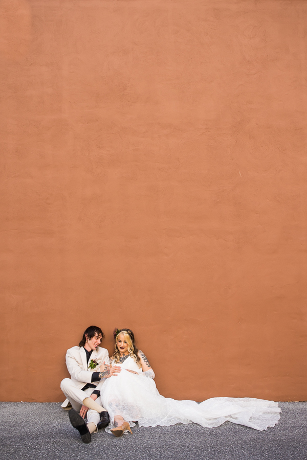 image of the bride and groom sitting against the terracotta colored wall in the parking lot outside of the cork factory hotel 
