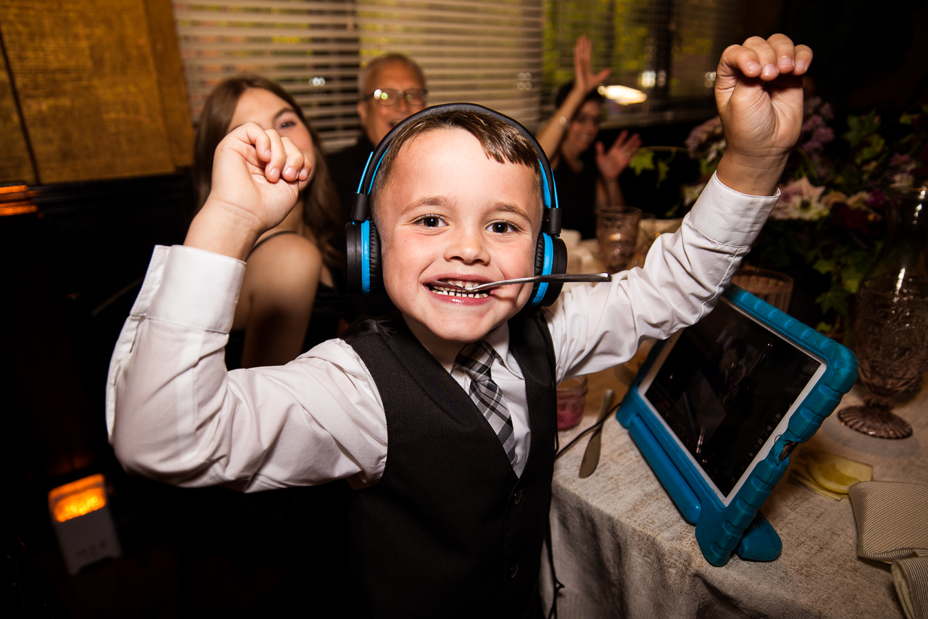 image of a kid with his hands in the air as he has headphones on and a spoon in his mouth during the wedding reception 