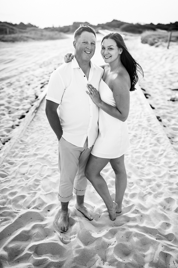 traditional black and white image of the couple as they stand together in the sand during their beach engagement session 