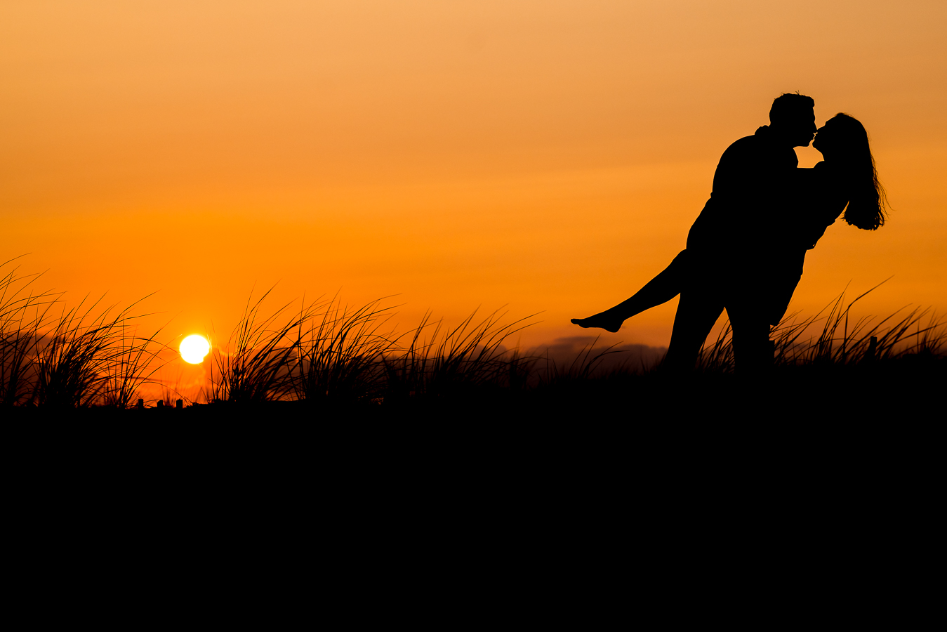 NJ Shore Engagement photographer, lisa rhinehart, captures this silhouetted image of the couple kissing each other as the vibrant orange sun is setting behind them 