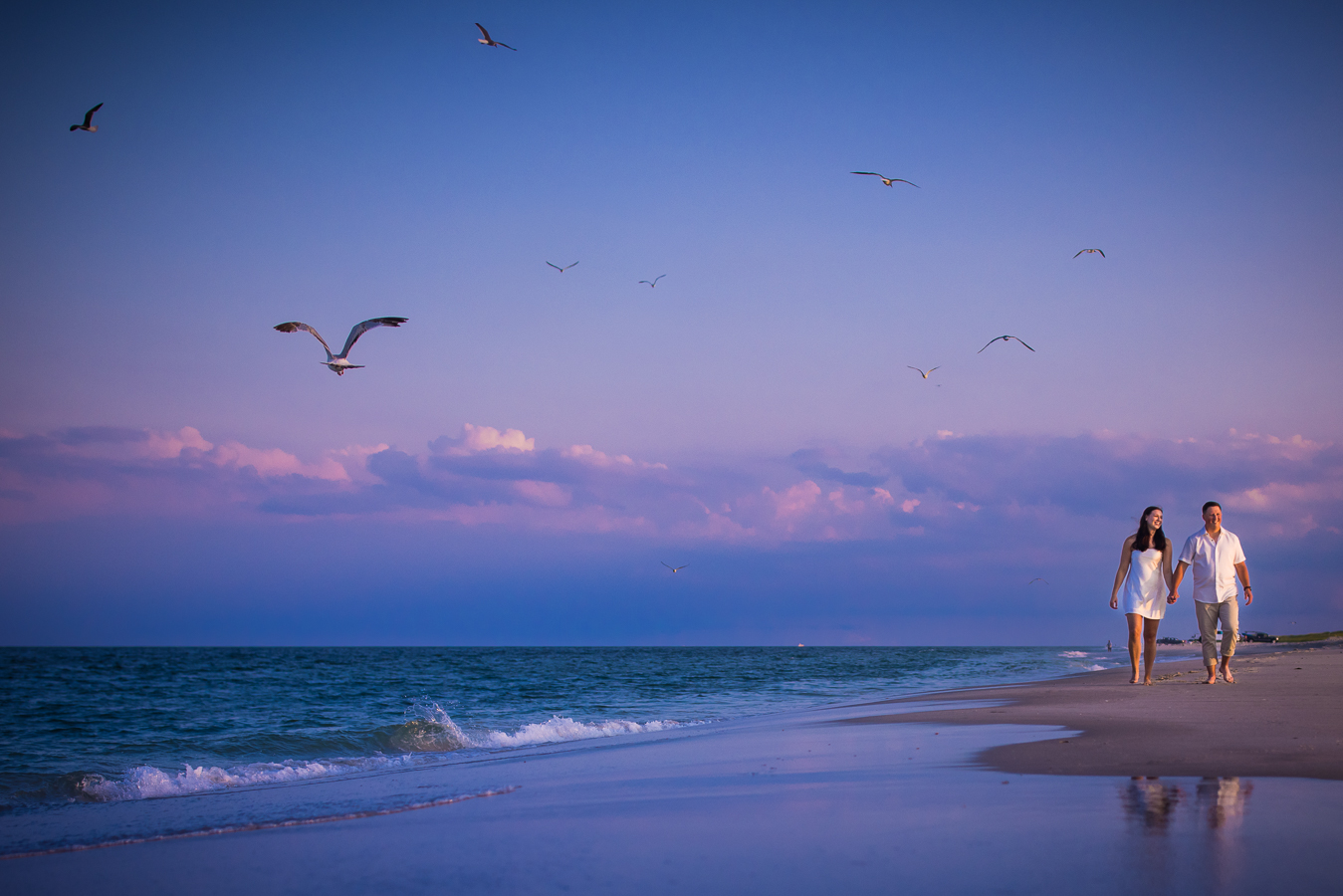vibrant, colorful image of the couple as they walk hand and hand on the sand watching the seagulls fly around them during their NJ Shore Engagement