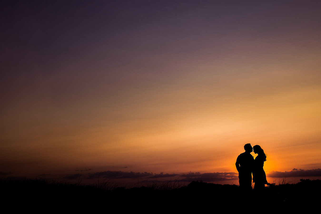 NJ Shore Engagement photographer, lisa rhinehart, captures this stunning colorful, vibrant image of the newly engaged couple standing with each other as the sun sets on the beach 