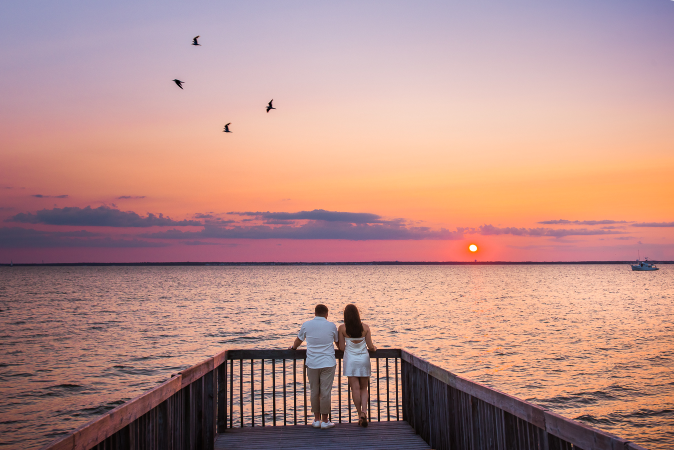 new jersey photographer, lisa rhinehart, captures this fun image of the couple watching the sunset together on the dock as the seagulls fly around them 