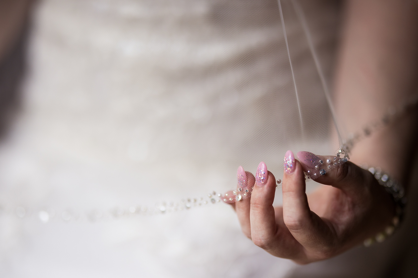 creative, unique image of the bride as she holds her veil and shows off the beading and her pink sparkley nails 