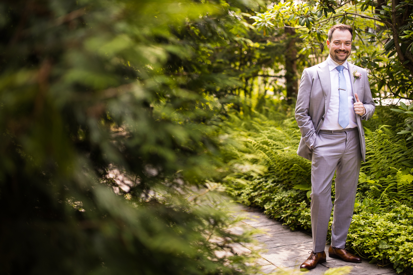 Holly Hedge Estate Wedding Photographer, lisa rhinehart, captures this image of the groom as he stands amongst the greenery smiling at the camera before his wedding ceremony 