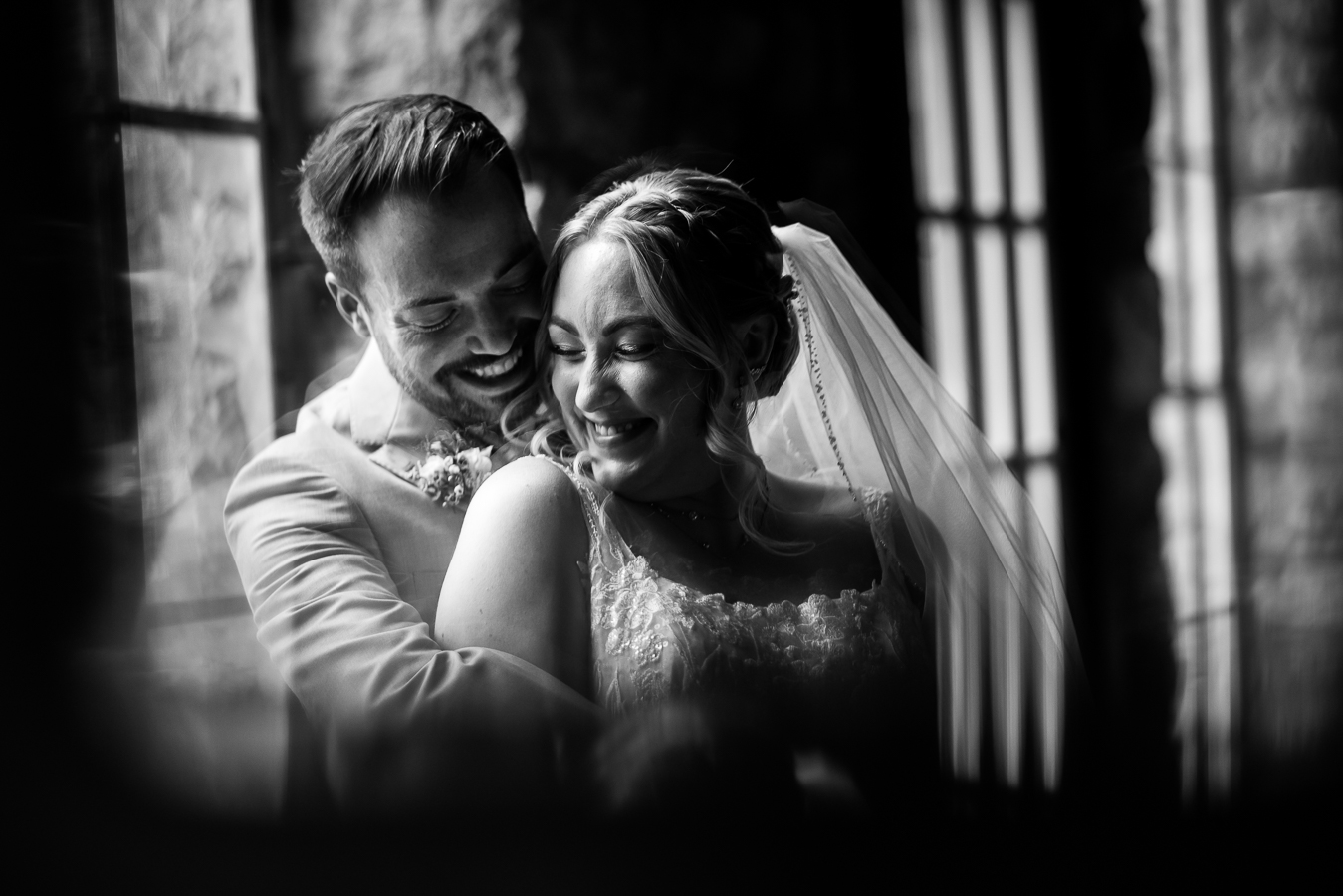 Holly Hedge Estate Wedding Photographer, lisa rhinehart, captures this unique, creative black and white image of the bride and groom hugging one another and smiling captured through the piano glass