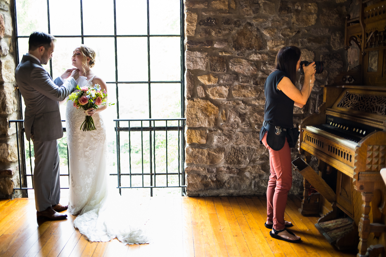 behind the scenes image of lisa rhinehart capturing the couples first look through the glass on the piano 