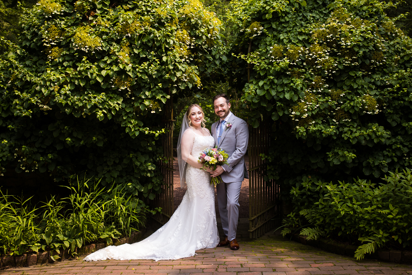 traditional portrait photographer, lisa rhinehart, captures this image of the bride and groom standing with each other in front of the gateway surrounded by lush greenery