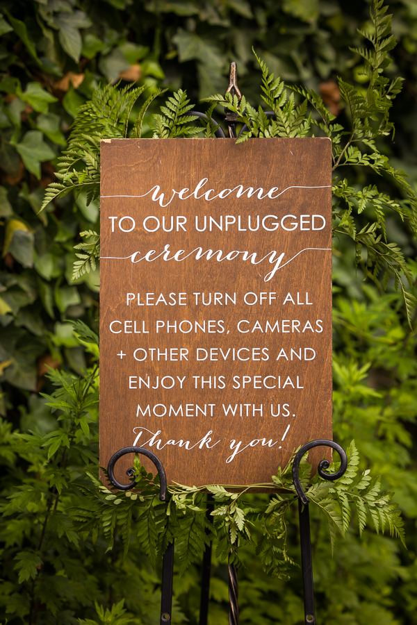 image of their wooden unplugged wedding ceremony sign surrounded by greenery