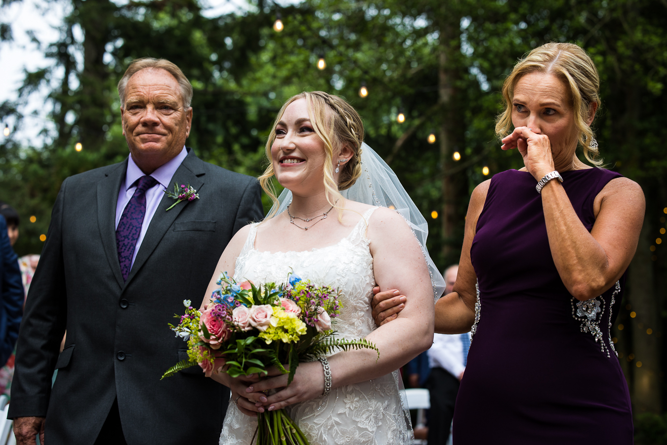candid image of the bride walking down the aisle with both her mom and dad as mom starts to tear up as they walk down the aisle 