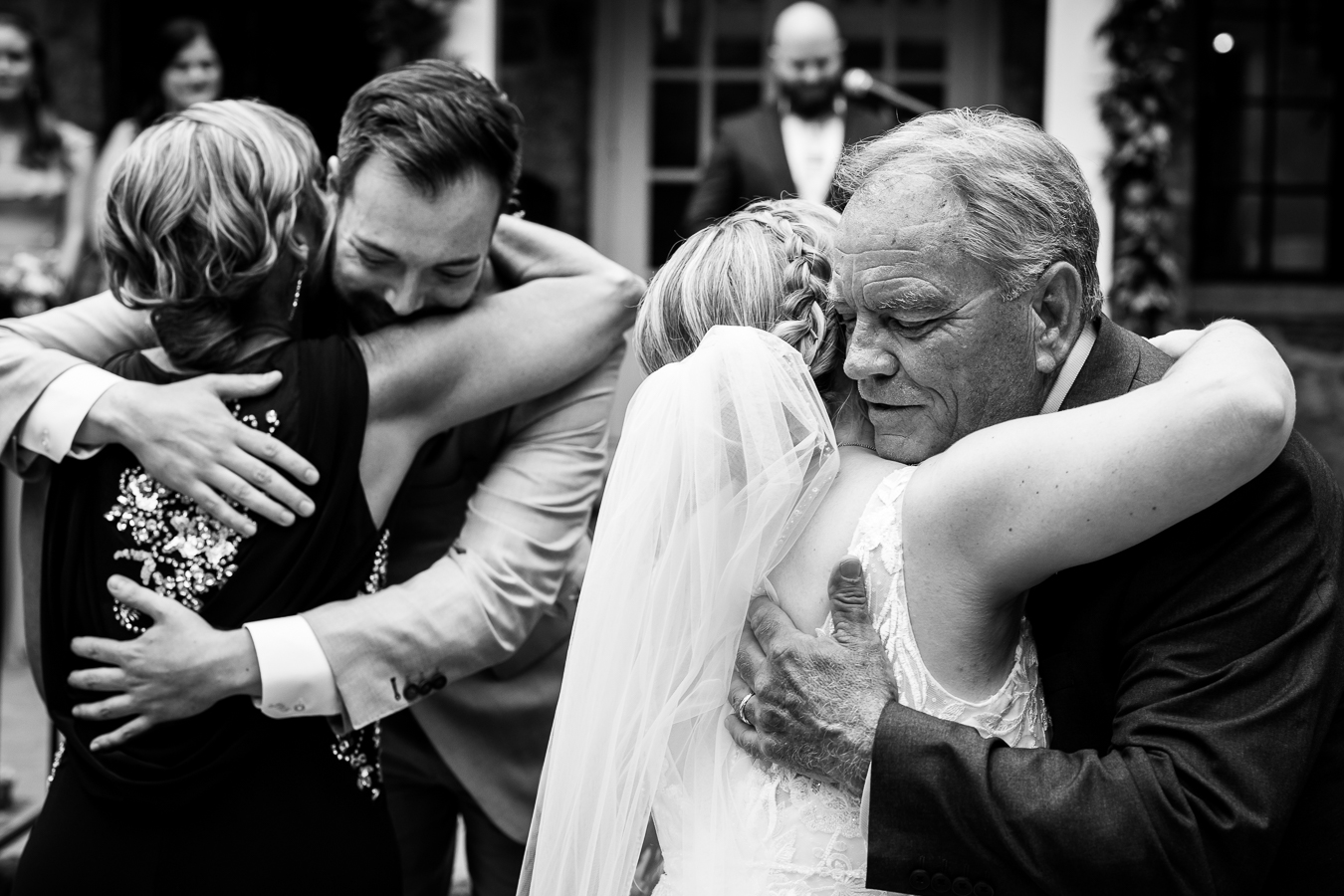 Holly Hedge Estate Wedding Photographer, rhinehart photography, captures this black and white image of the bride hugging her dad and the mom hugging the groom 