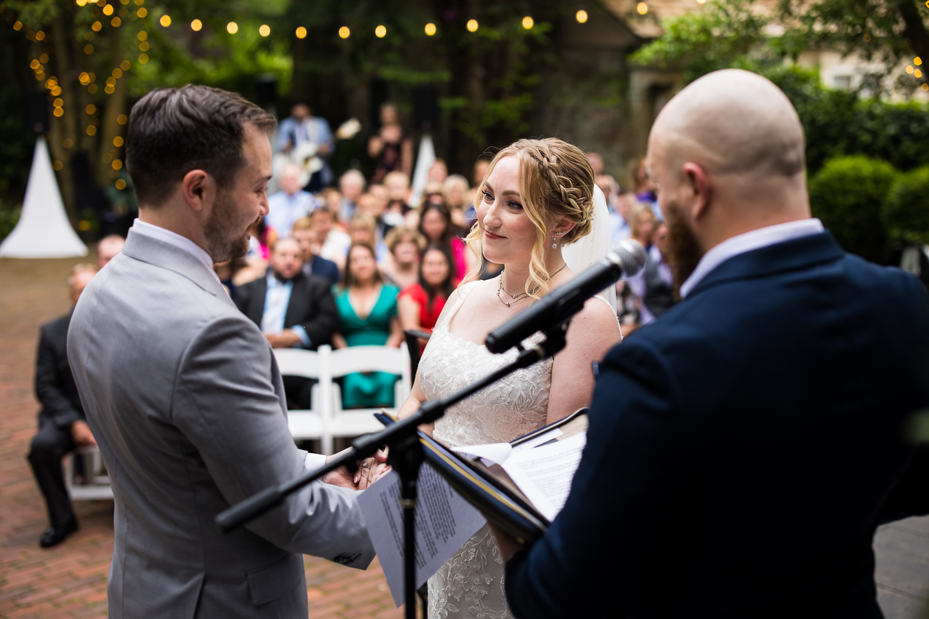 wedding photographer, lisa rhinehart, captures this image of the bride and the groom as they hold hands and smile at one another during their wedding ceremony at their venue in new hope, pa 