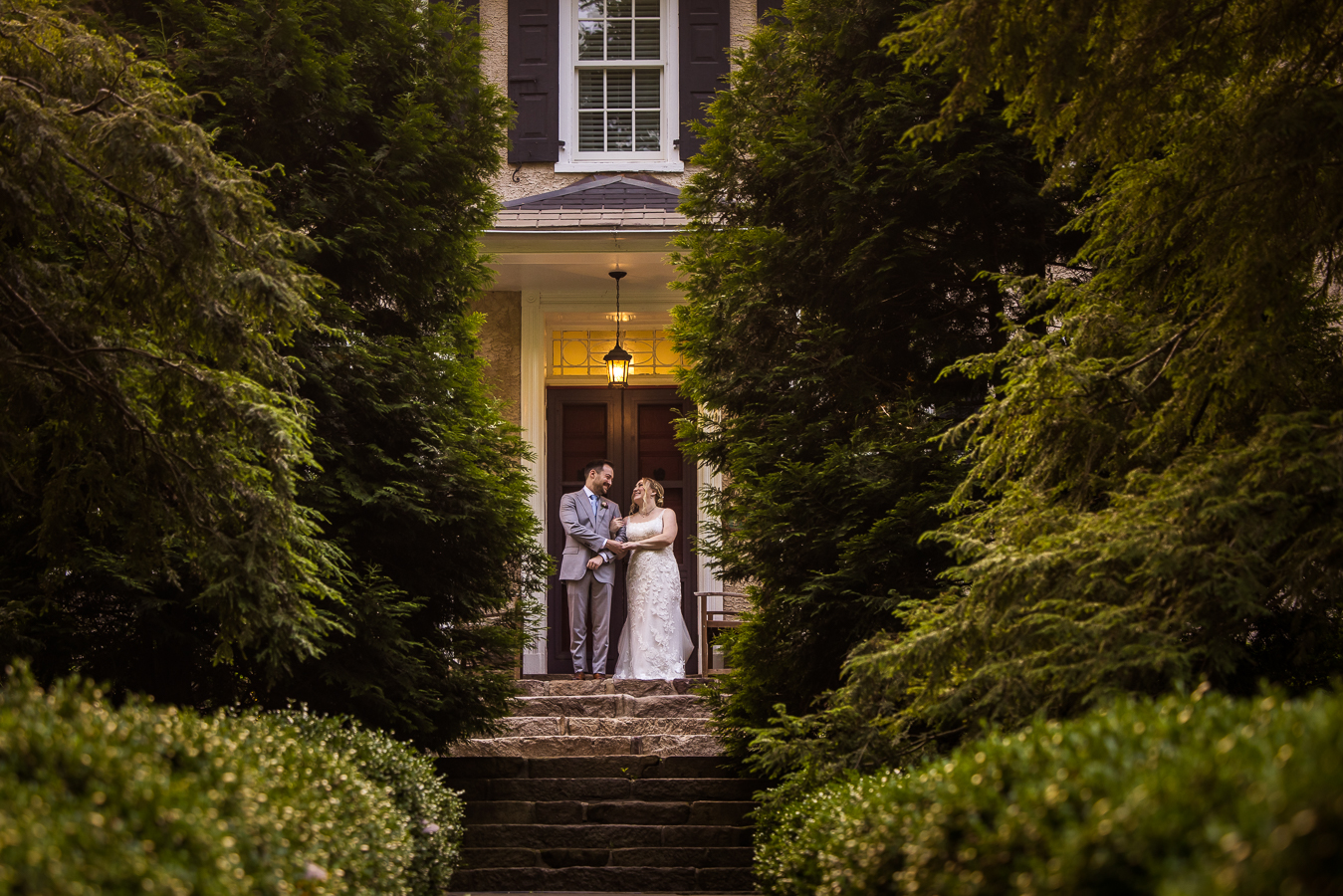 creative, unique image of the bride and groom as they embrace each other in front of their wedding venue framed by the lush greenery in new hope pa 