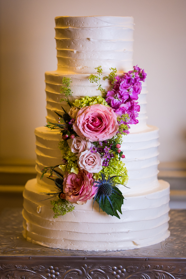vibrant, colorful image of the white wedding cake with vibrant colorful florals wrapping around it 