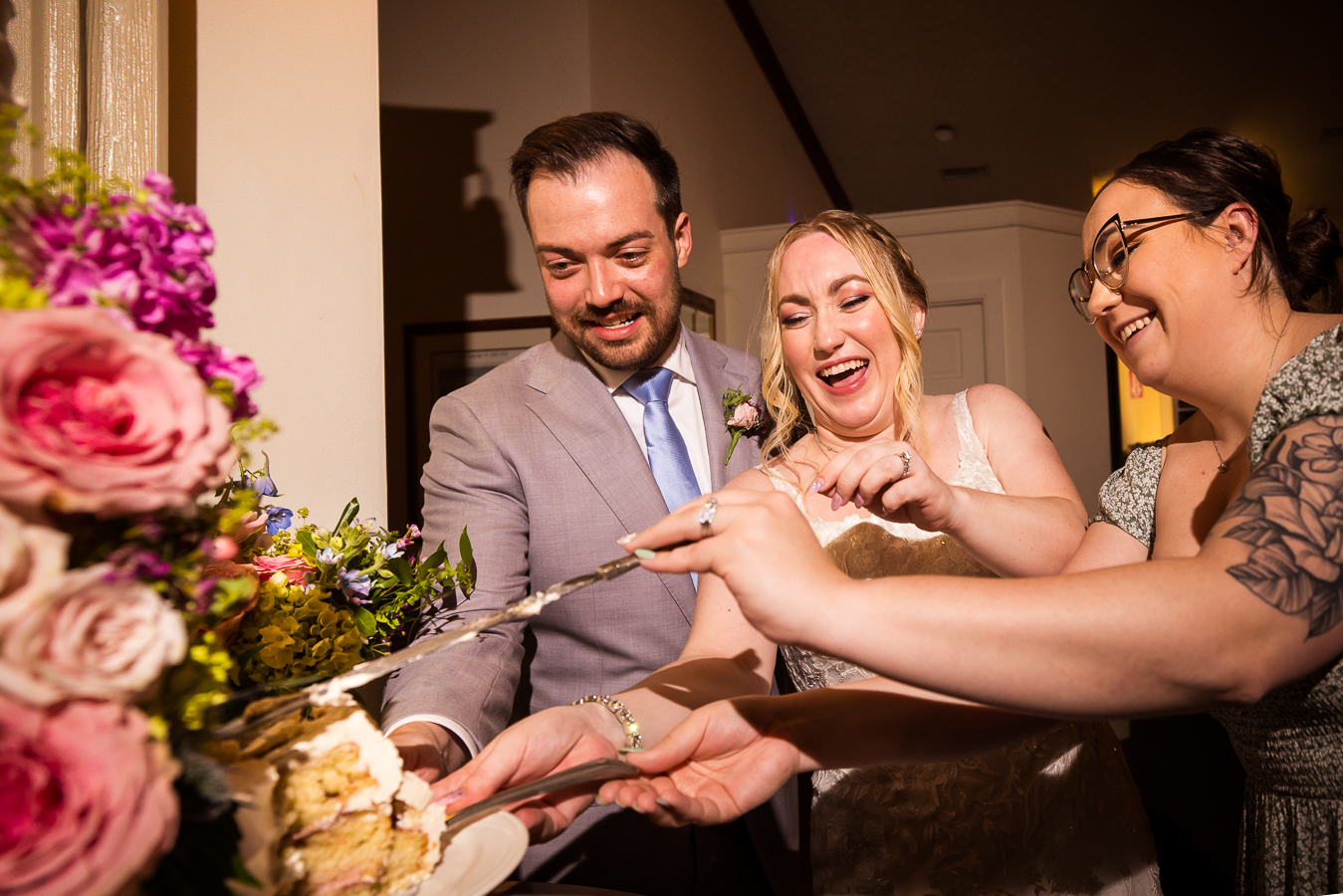 image of the bride and groom as they cut their wedding cake with the help of hollyhedge staff