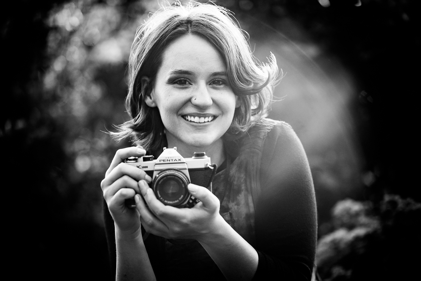 black and white image of this creative senior holding her camera and smiling at the camera