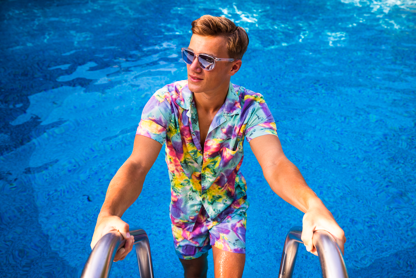 Creative Senior Portrait Photographer, lisa rhinehart, captures this vibrant, colorful, unique summer senior portrait session as he is dressed in a vibrant top and bottoms with sunglasses on for this outdoor senior session